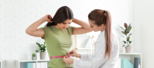 Nutritionist measuring waist of young woman in weight loss clinic