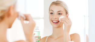 smiling young woman applying lotion to cotton disc for washing her face at bathroom