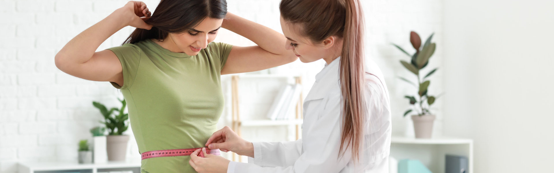 Nutritionist measuring waist of young woman in weight loss clinic