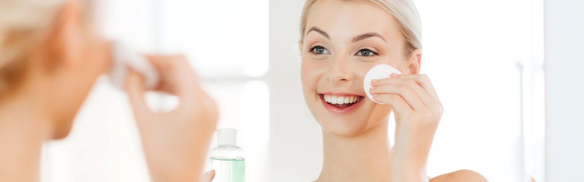 smiling young woman applying lotion to cotton disc for washing her face at bathroom